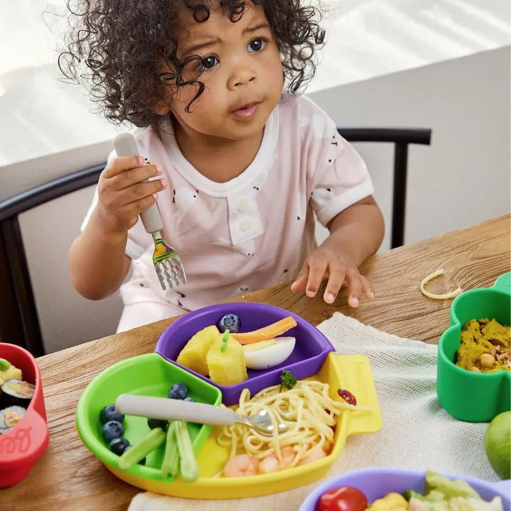 Toddler eating from a Beemymagic silicone heart plate with fork at a wooden table